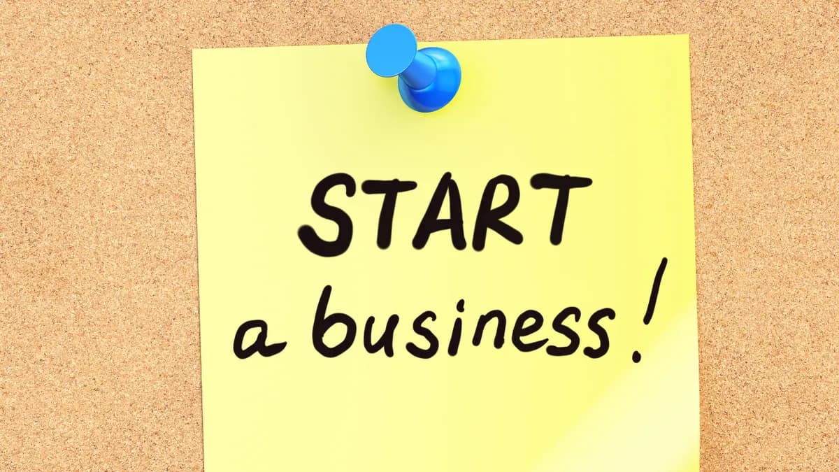 A yellow sticky note reading 'Start a business\!' pinned to a corkboard